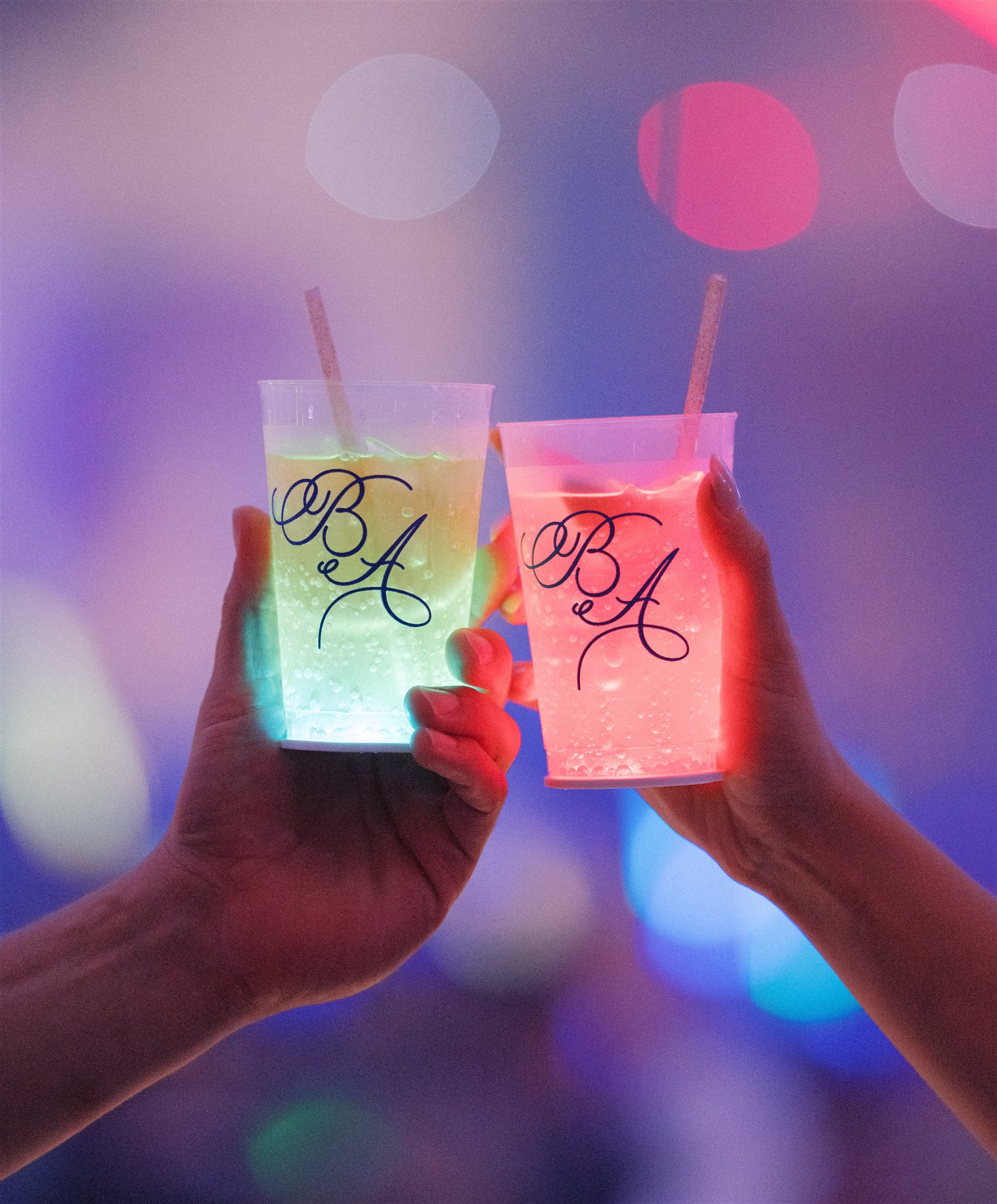 A close-up of two plastic frost flex cups with a custom monogram. An LED coaster stuck to the bottom of each cup lights them up with color.