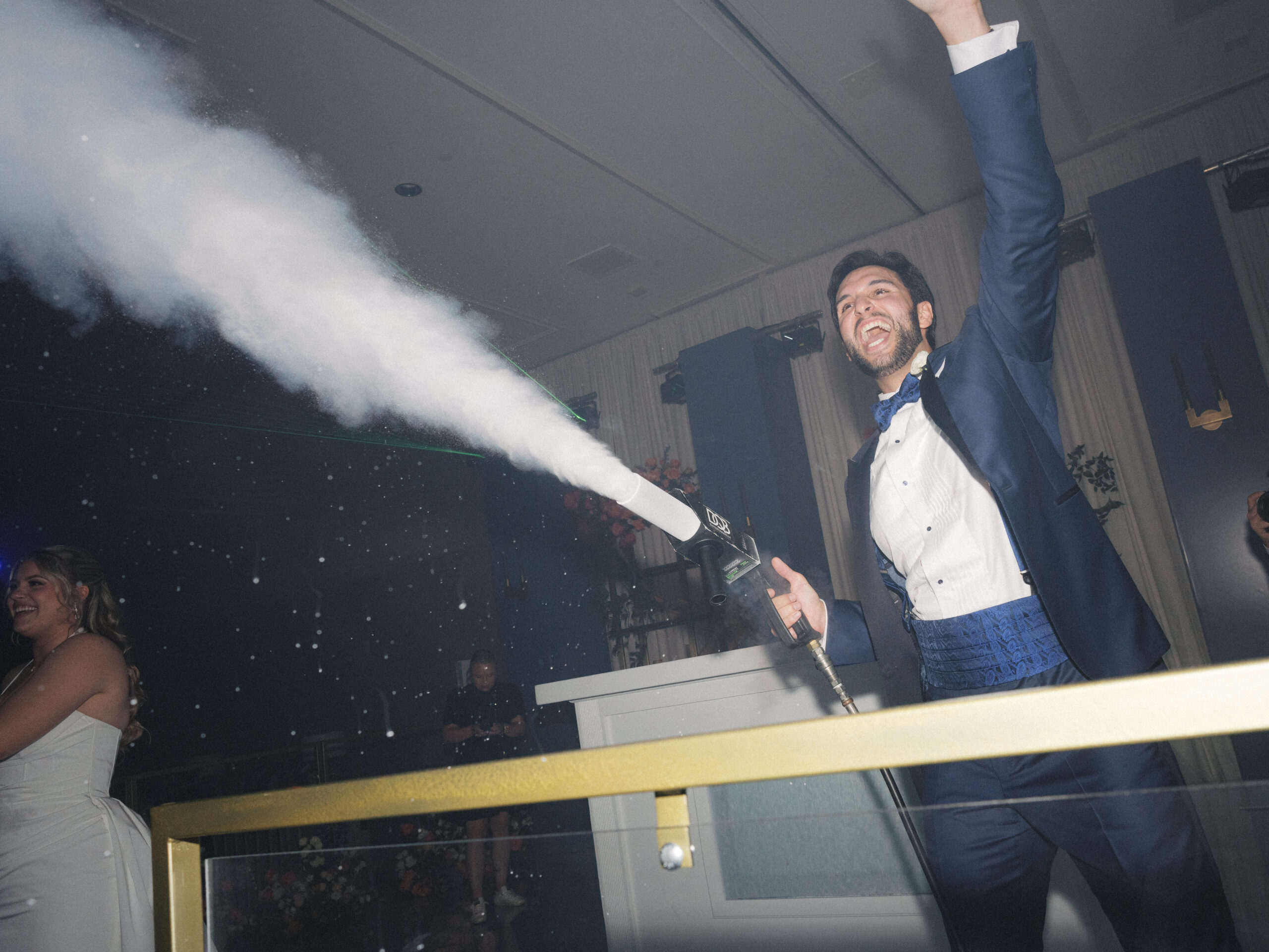 A groom laughs as he shoots air from a C02 gun over the dance floor at his wedding.