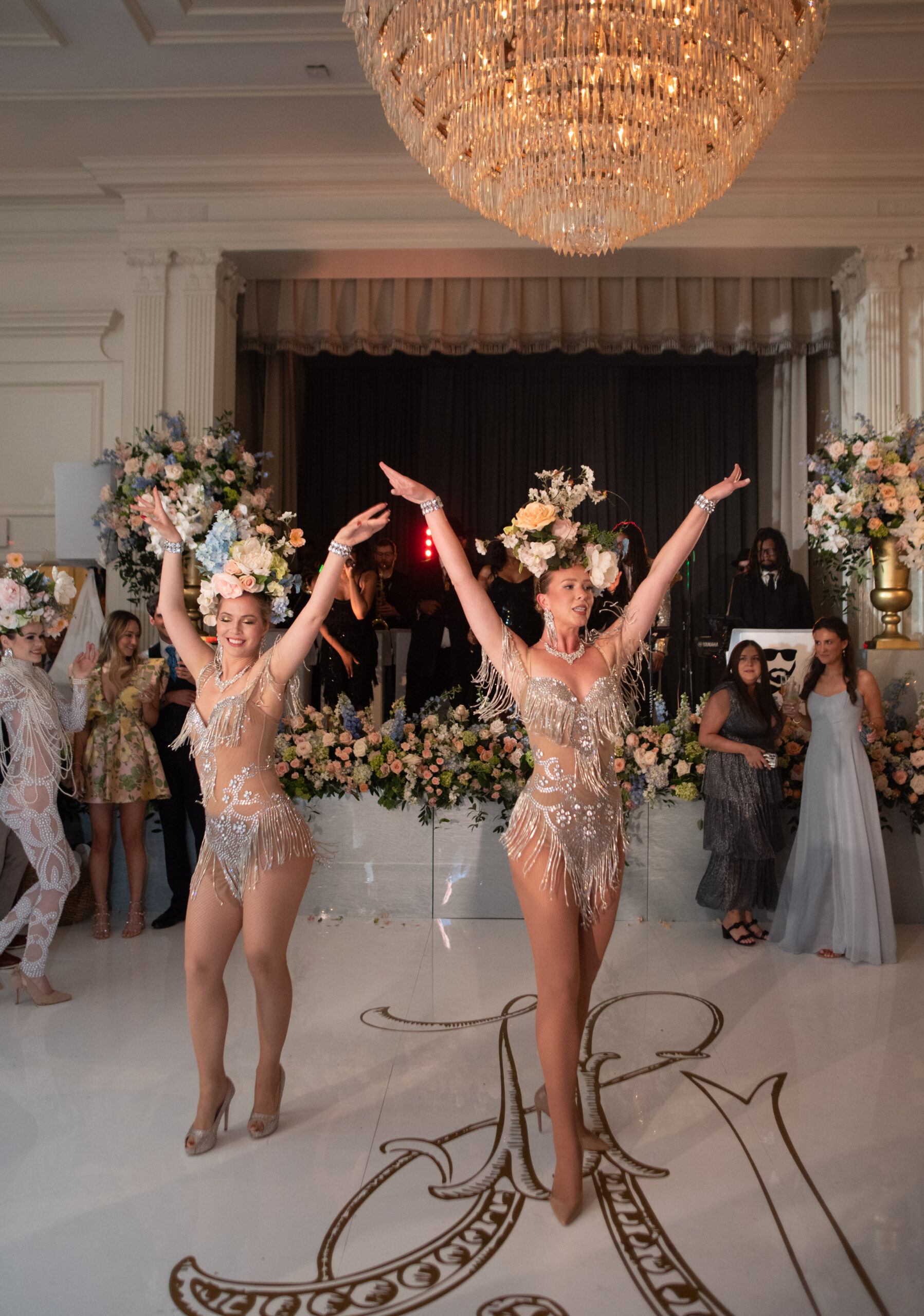 Two dancers in sequin fringe bodysuits and floral headpieces provide entertainment at a wedding reception.