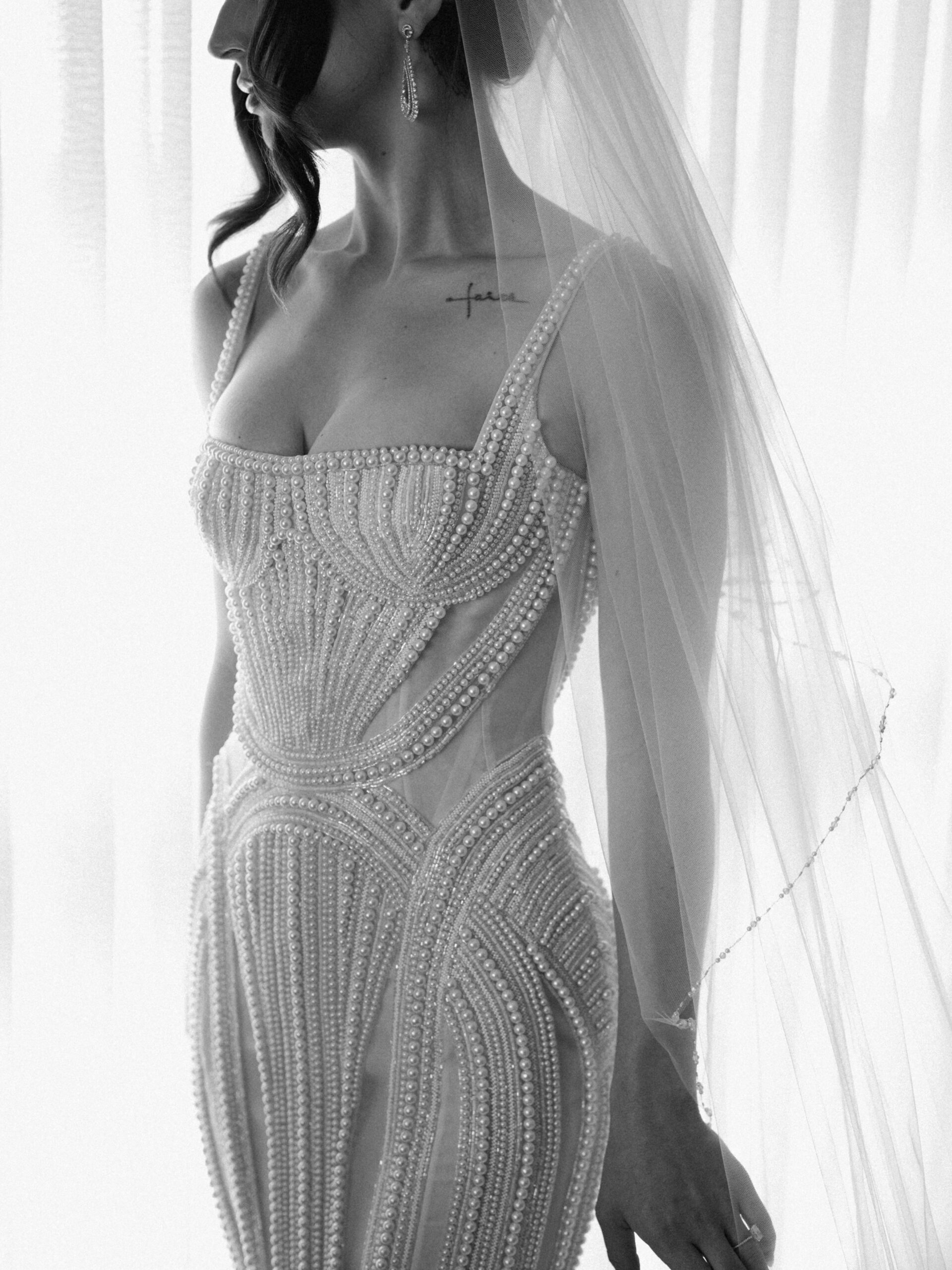 A black and white glamour portrait of a bride wearing a gown intricately beaded with pearls.