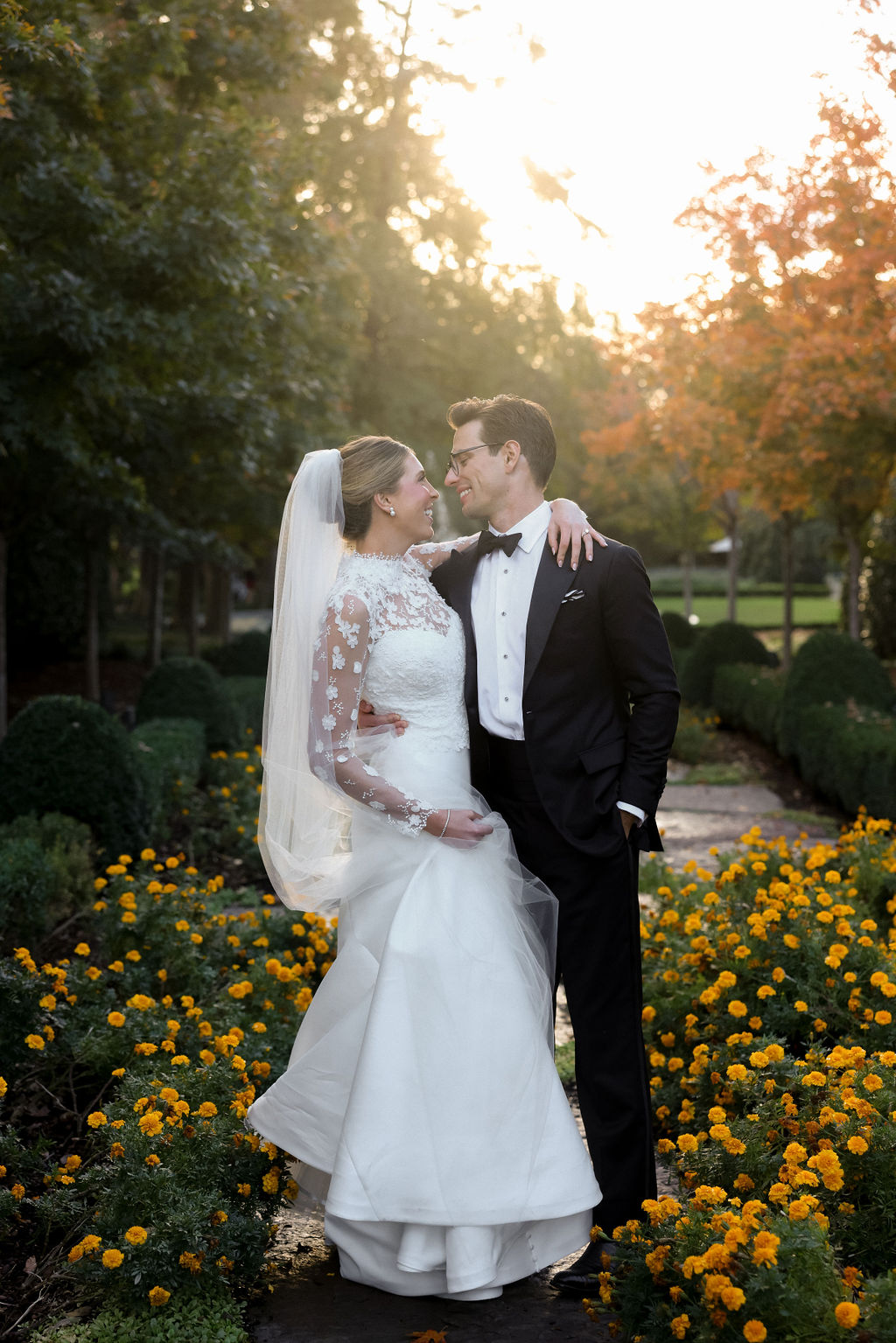 A bride and groom smile as they hold each other close, bathed in a golden hour glow.