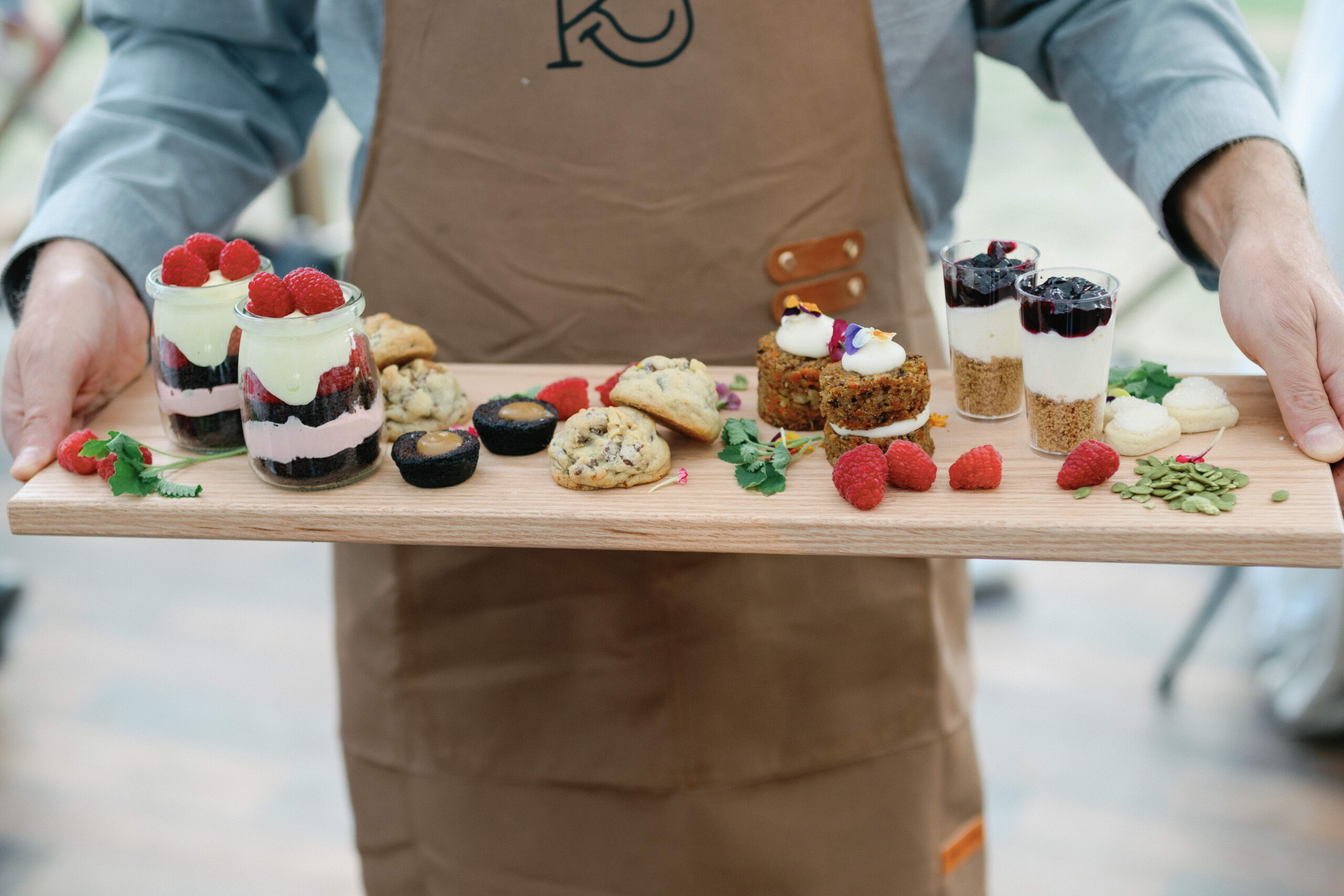 A waiter poses with a rustic board of assorted desserts, showcasing the food and beverage vision for a ranch wedding.